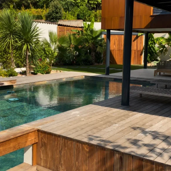 Piscine, terrasse en bois et pool house dans un jardin aux palmiers