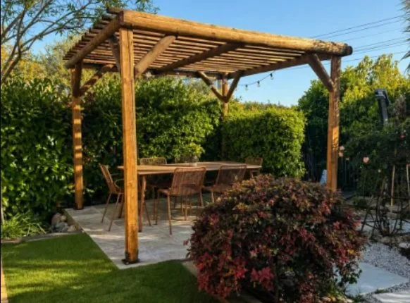 Pergola en bois abritant une table, pelouse synthétique et haie de laurier
